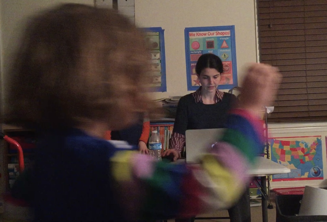 A woman works on a computer while a child walks in front of her.